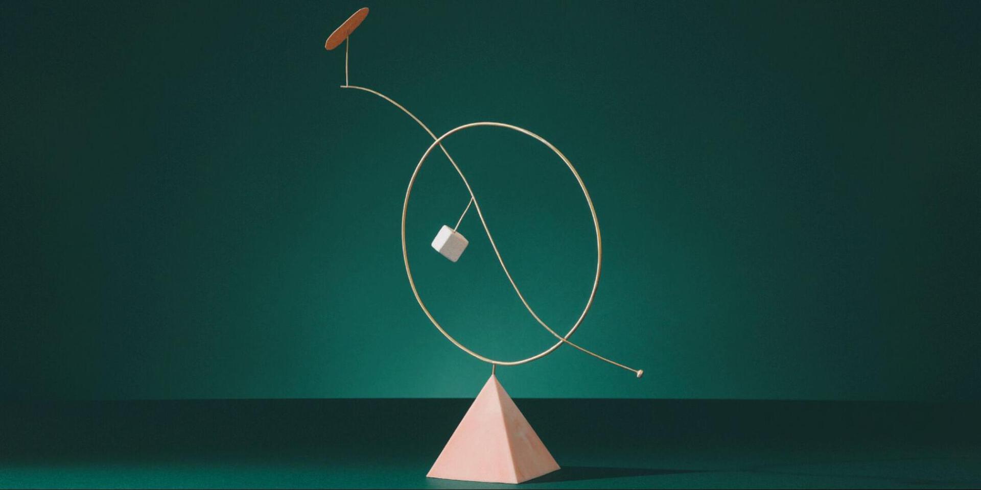 A wire circle with a dangling cube balances on a pyramid.