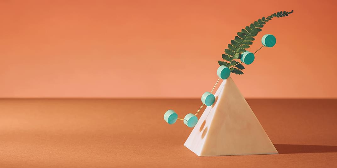 Linked cylinders rest against a pyramid with a fern leaf sprouting from the top. 