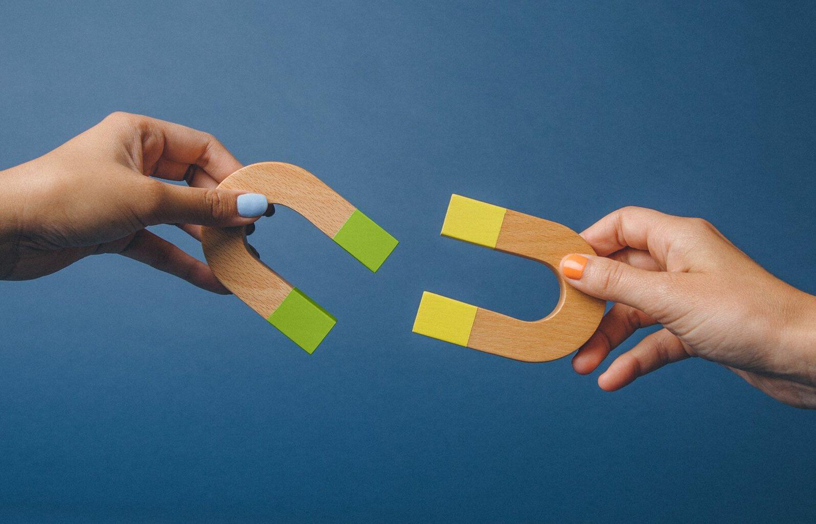 Hands holding U shaped magnets on orange background