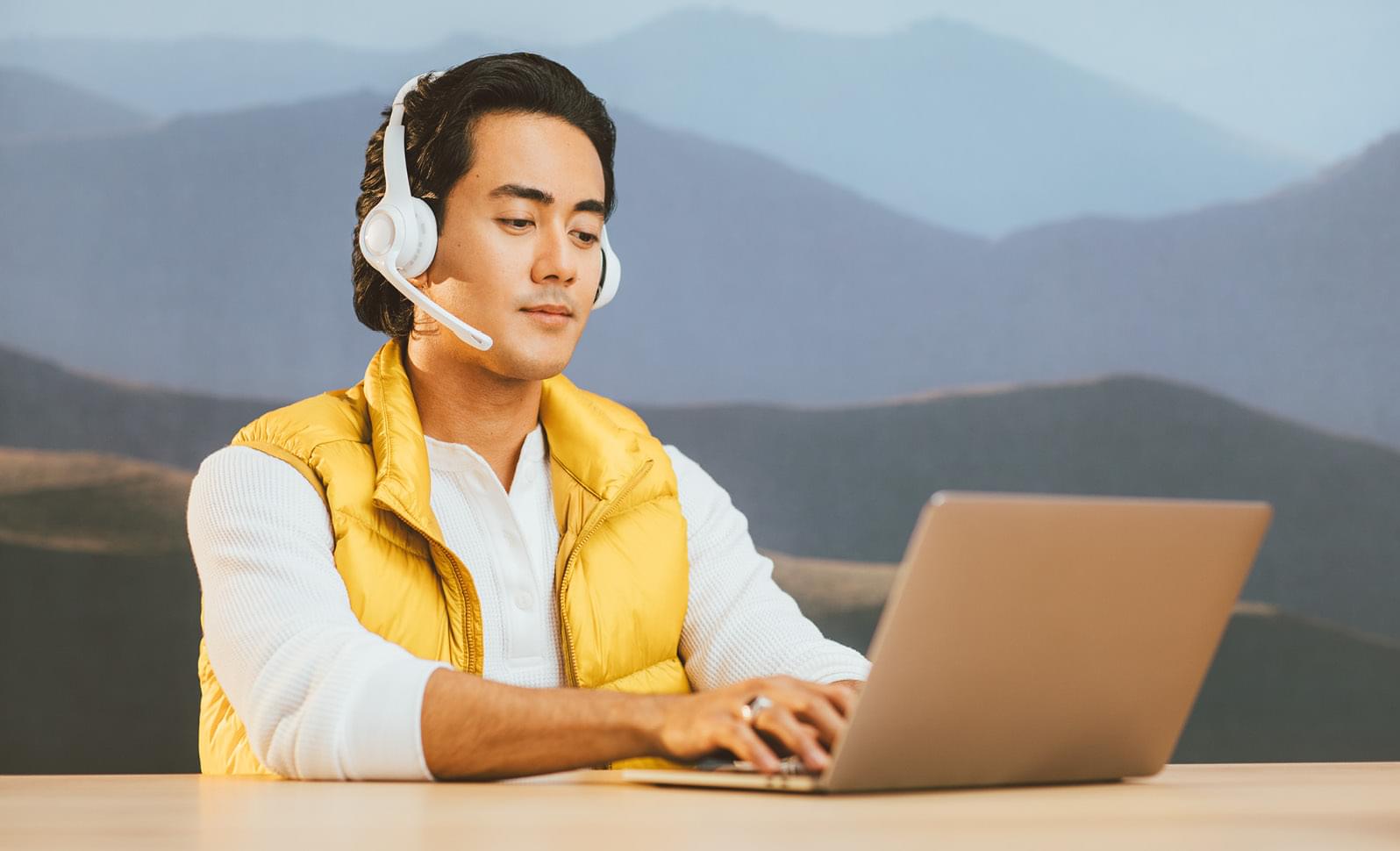 A man in a yellow vest works on his laptop.