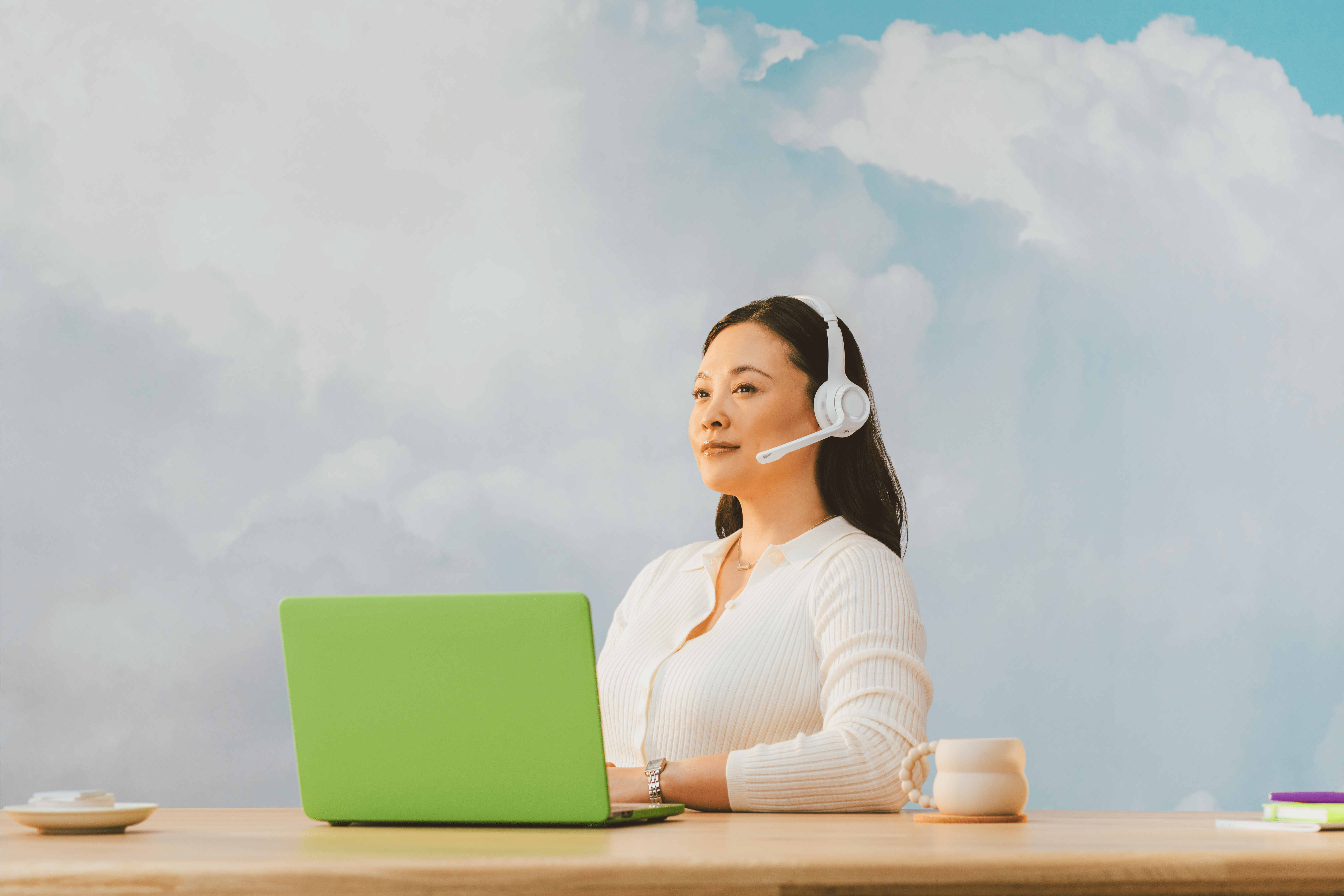 A customer support agent wearing a headset sits before a sky print background