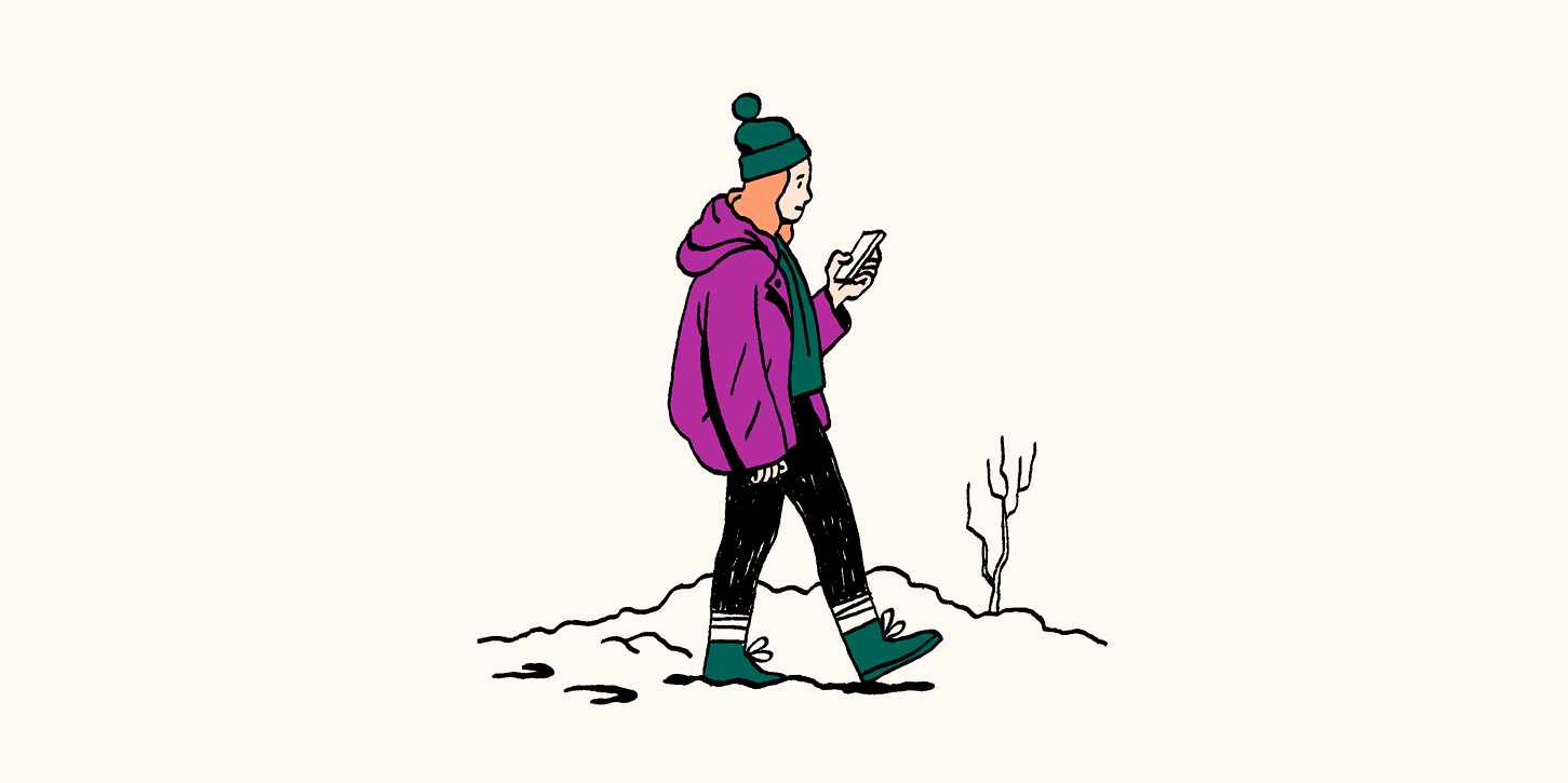 A woman is on her phone while walking through the wilderness.