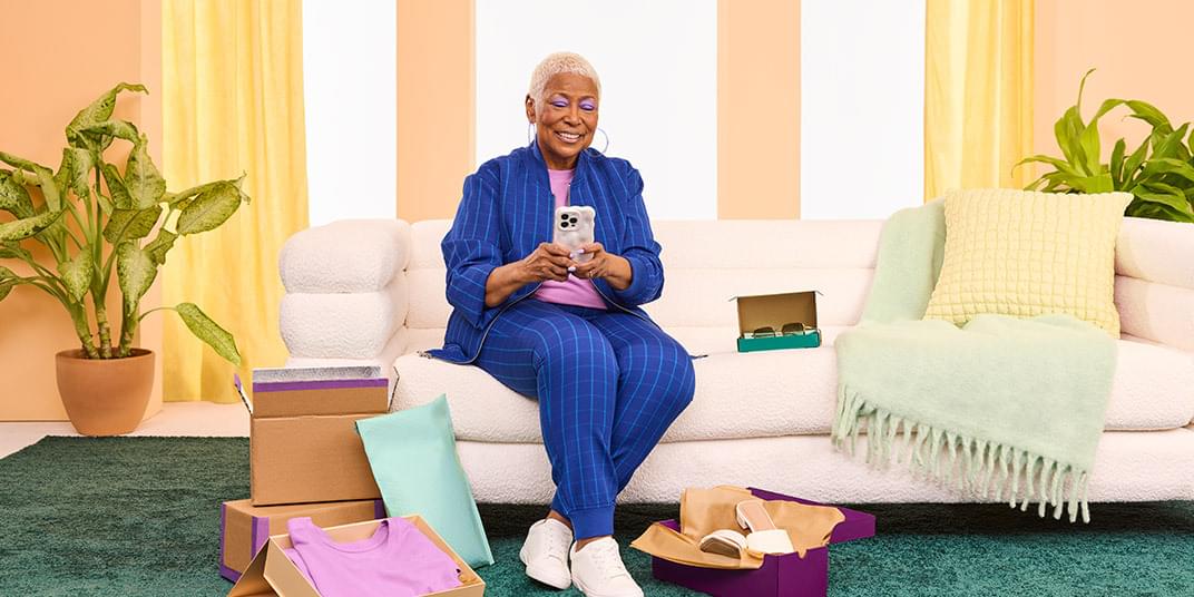 A woman sits on the couch and reads about the differences between customer success and customer experience on her phone.