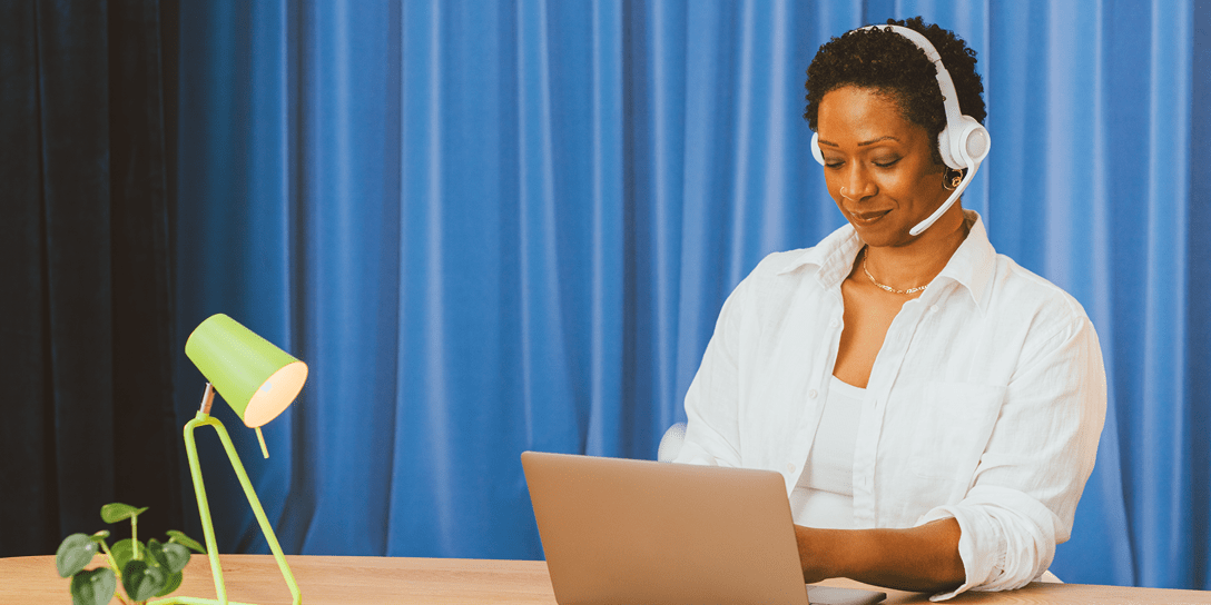 A person with a headset sits at a desk and sends sales follow-up emails to prospective customers.