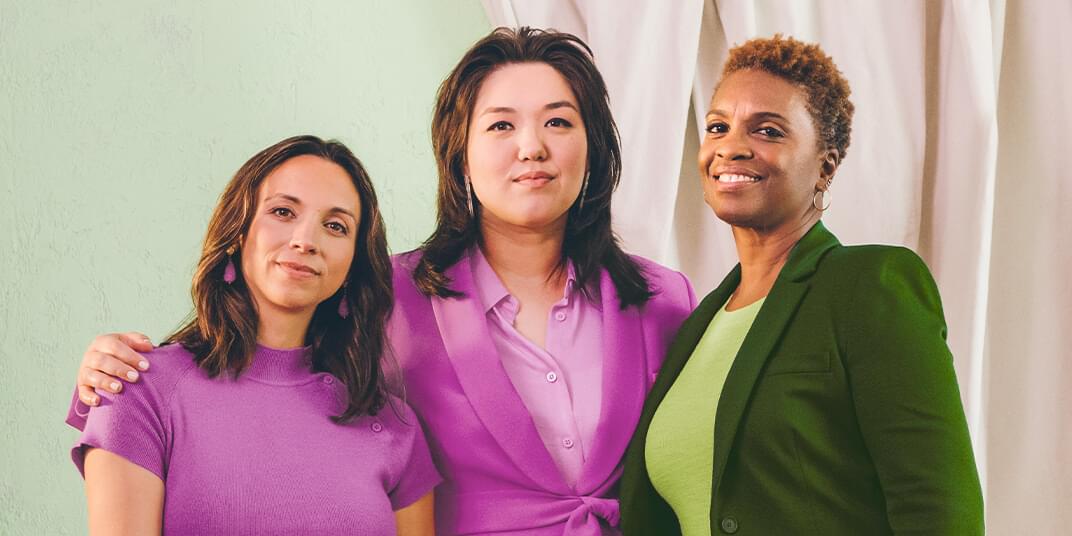 Three women in business casual clothing stand in front of the camera.