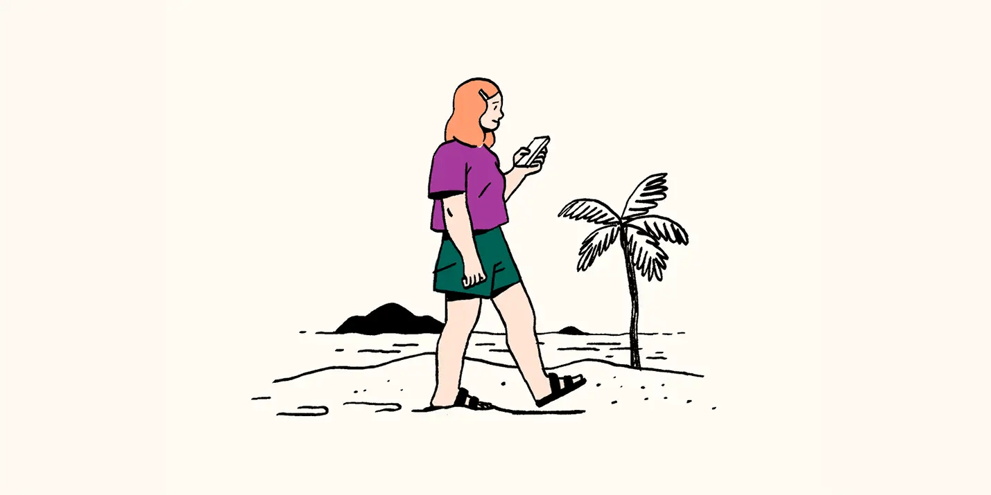 A woman walks on the beach while on her smartphone.