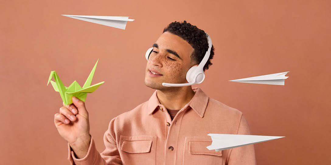 A man wearing a headset stares intently at a paper swan with paper airlines flying around him.