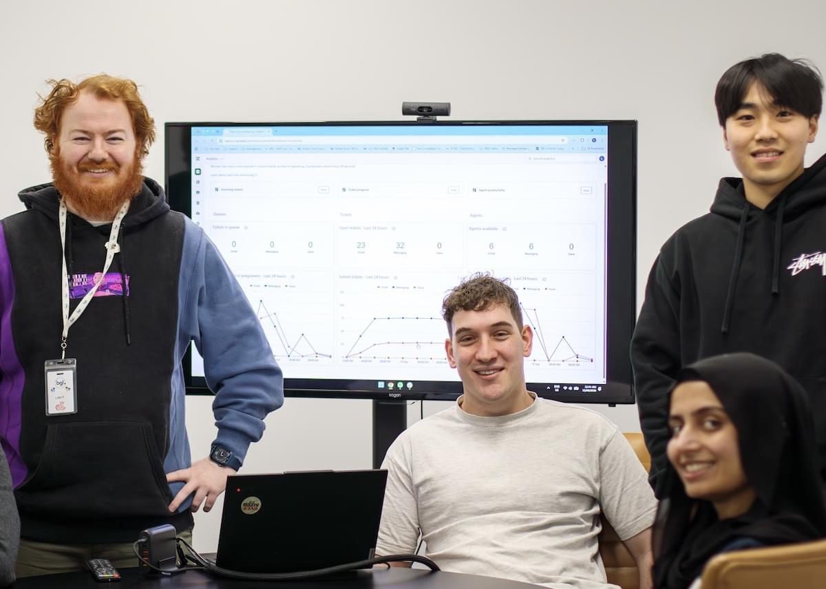 Four smiling BGL employees stand in front of a digital screen displaying graphs and charts