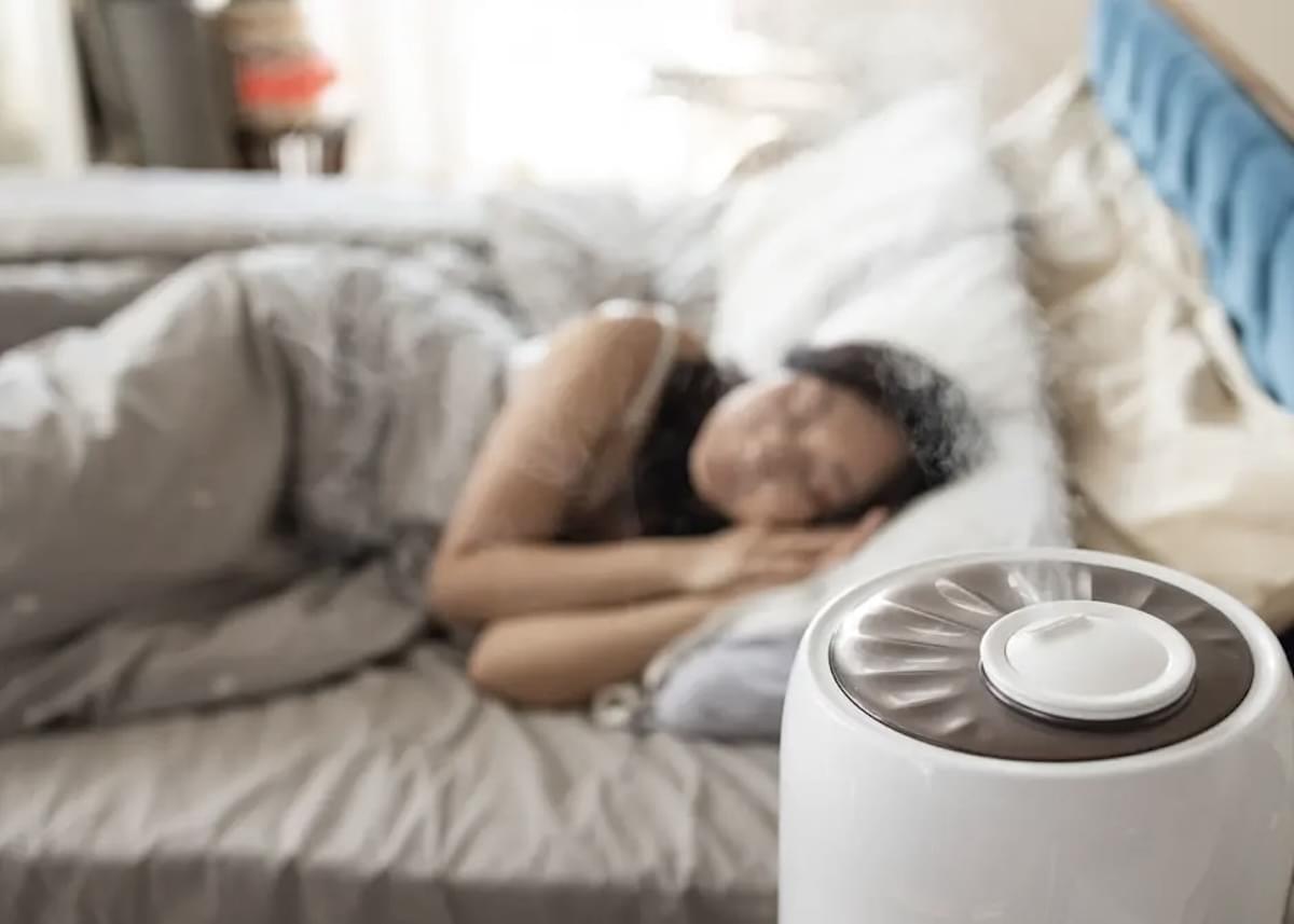 Mulher dormindo em sua cama com umidificador de ar funcionando