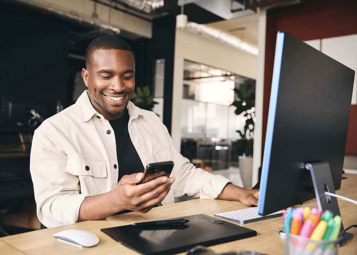 Smiling an at computer, looking at phone