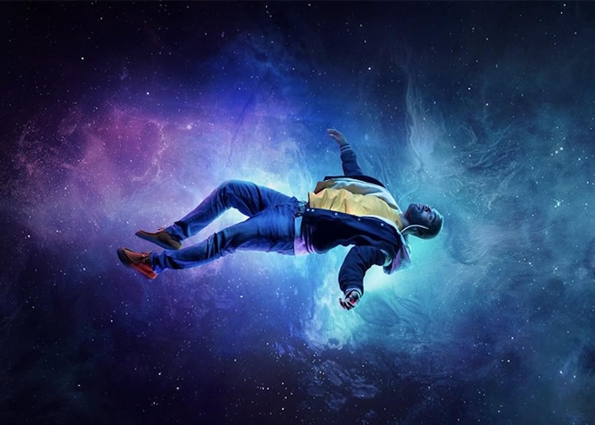 A man in a casual suit floats in a galaxy.