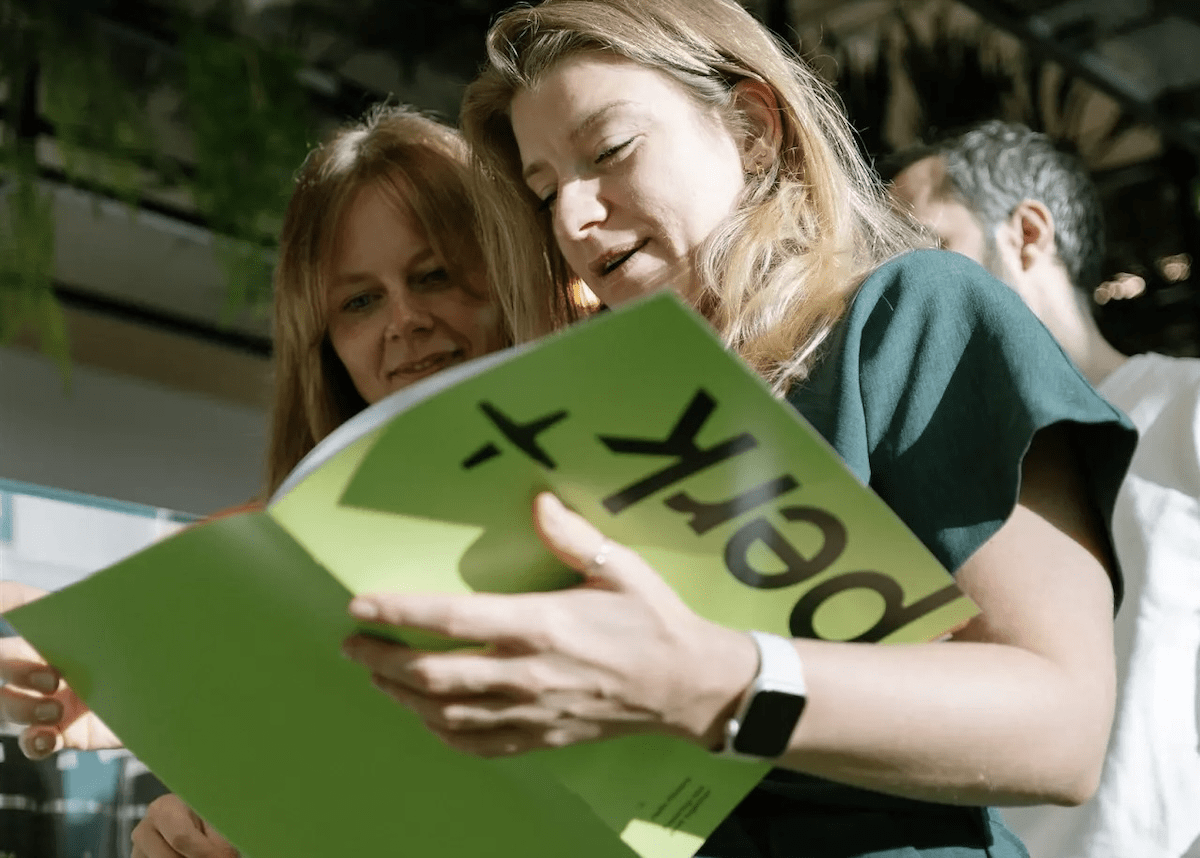 Two women read through a Perk brochure at a conference