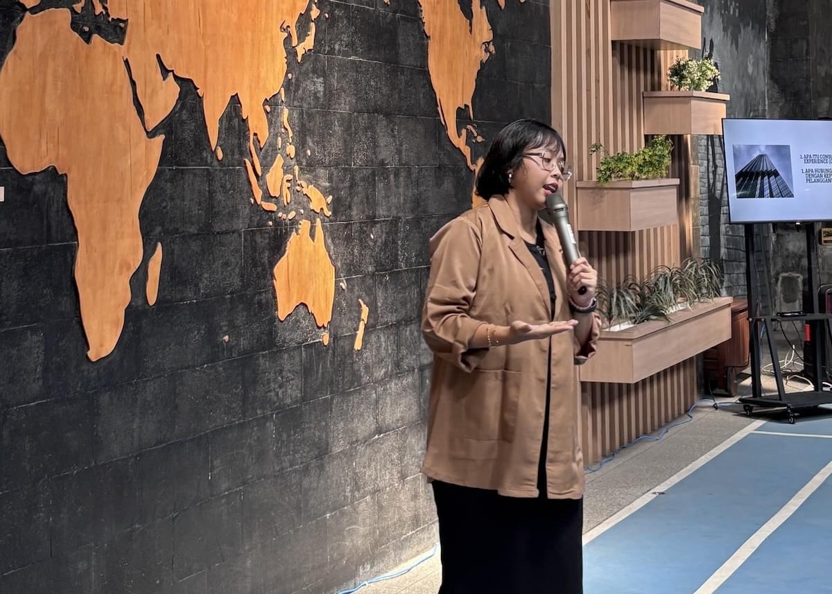 A woman with a microphone speaks inside Privy's office, with a wooden map of the world in the background