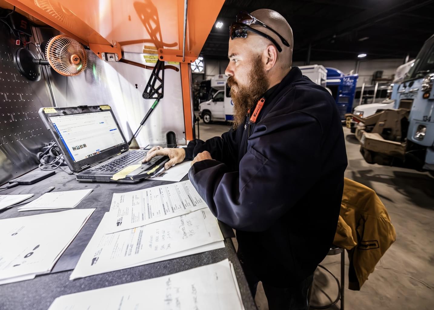 A bearded man in an auto workshop looks at the Shopmonkey website on his laptop.