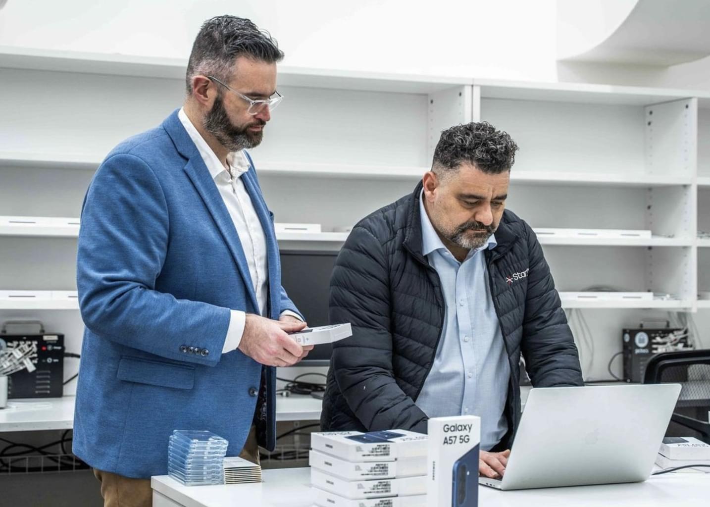 A Star21 employee and customer look at a laptop next to a stack of new mobile phones