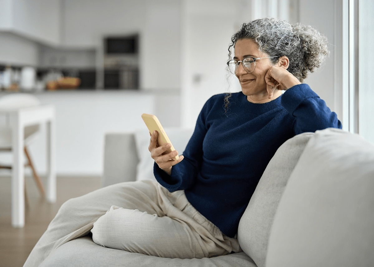 A middle-aged woman sits on her couch as she visits XP Health's website on her phone