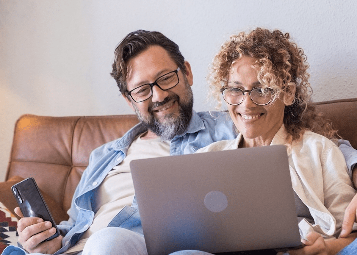 A middle-aged couple sits on their couch as they visit XP Health's website on their laptop