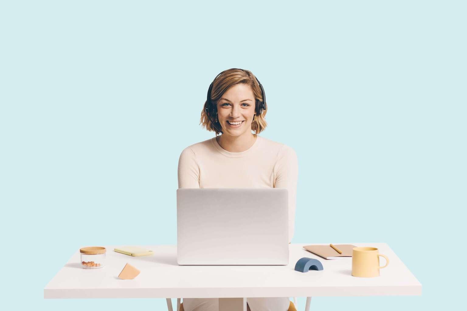 Support agent wearing headset sitting behind a desk with laptop and various items on the desk