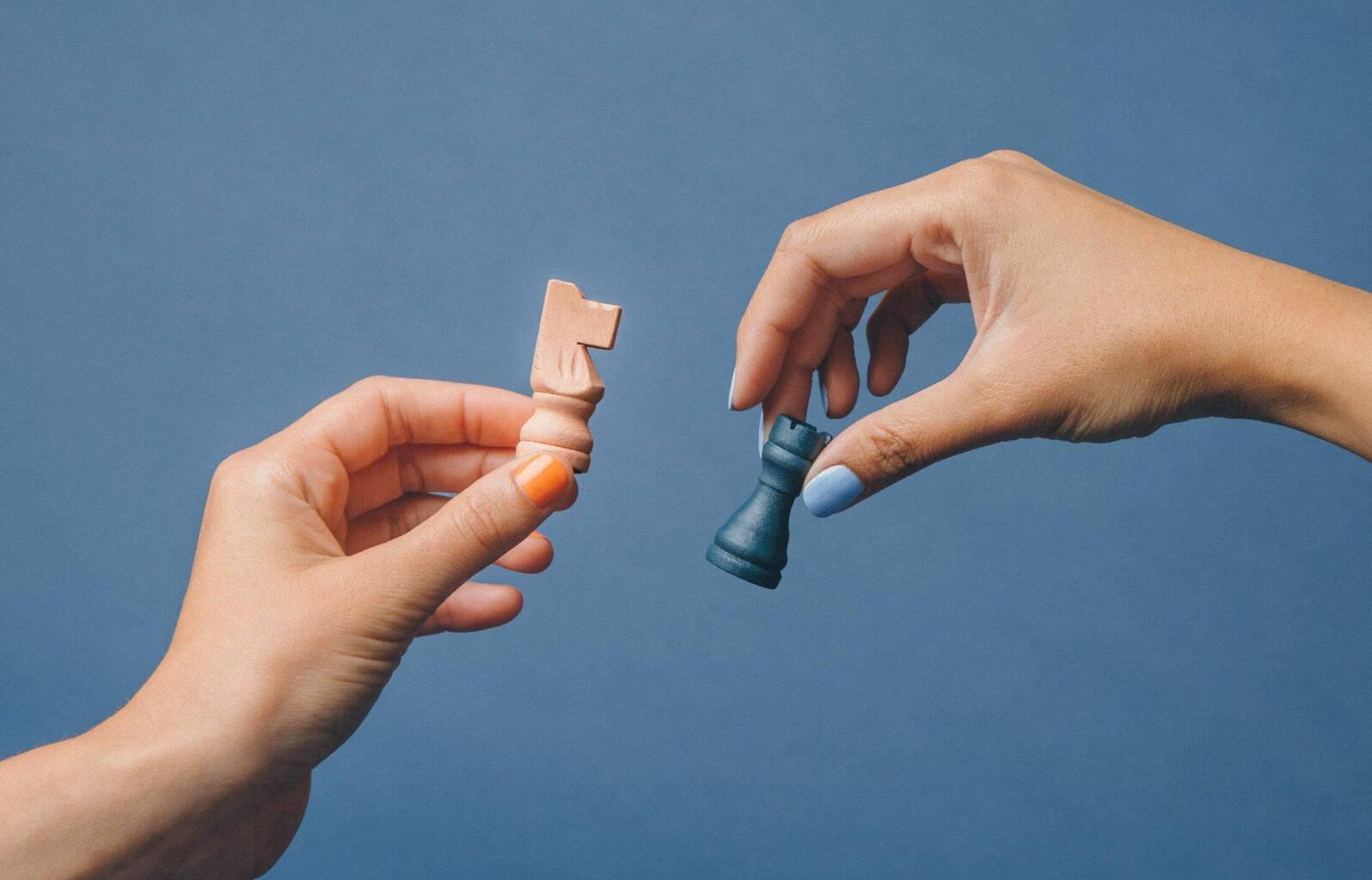 Two people each holding a chess piece zoomed in on their hands and the chess pieces in close detail