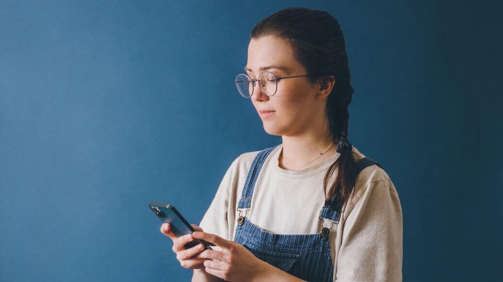 Young woman wearing overalls looking down at her cell phone