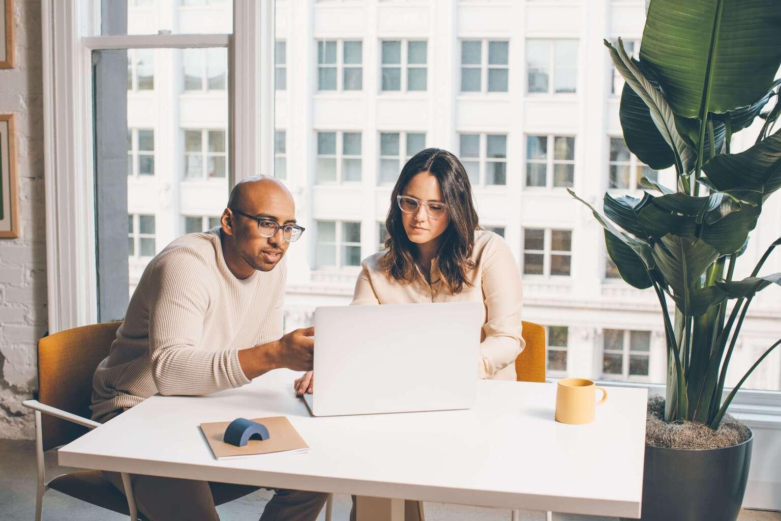 Two people huddling together around a laptop as if collaborating on a problem