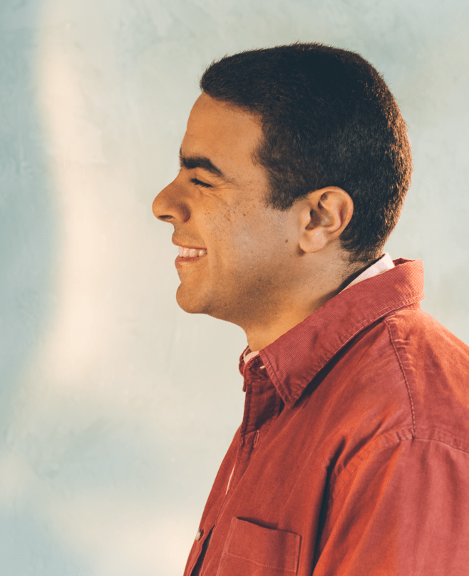 Photo: Portrait of young man smiling, wearing a red button-up shirt.