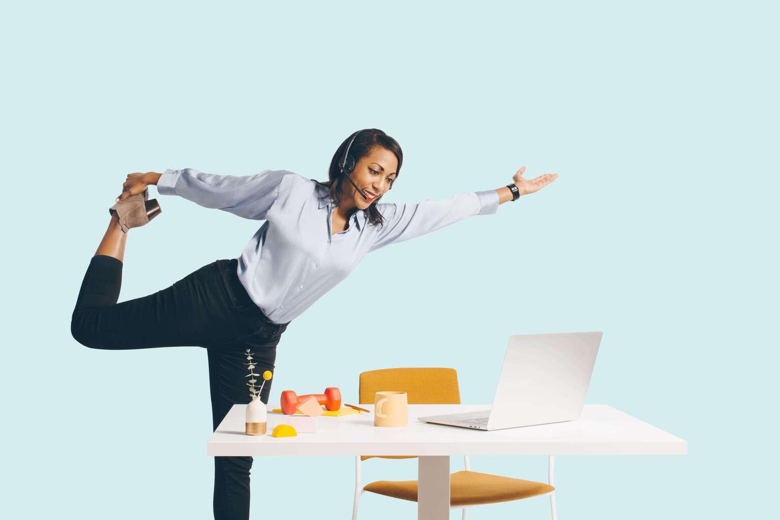 Woman standing at a work station with her leg stretched out behind her back in a yoga position, demonstrating flexibility and agility 